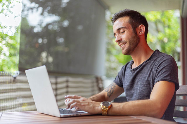 Man working remotely on a laptop outdoors, smiling and enjoying the fresh air.